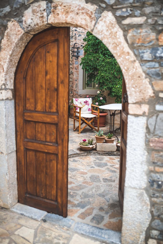 Charming courtyard scene viewed through an arched wooden doorway with stone walls.